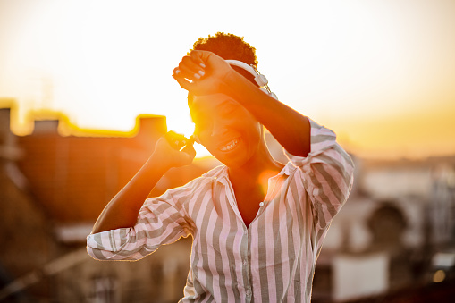 Photo of a young woman with headphones on the rooftop enjoying the sunset