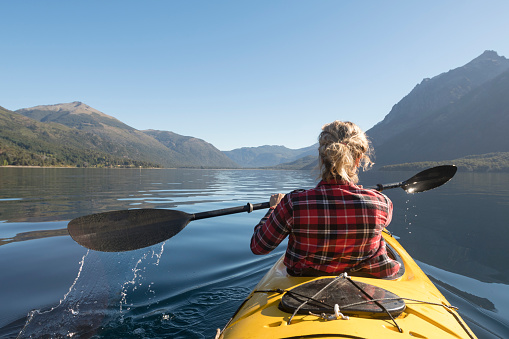 Beautiful woman Enjoying the lakes in her yellow kayak for her summer vacation trip through Patagonia.