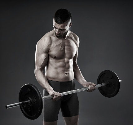 Young athletic man training with a barbell isolated on gray background