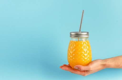 Healthy yellow smoothie jar with metal drinking straw on blue background. Zero waste.