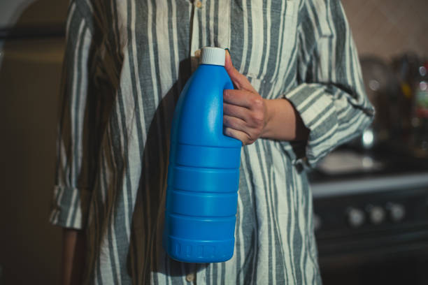 An unrecognizable person in striped shirt is posing with a bottle of bleach.