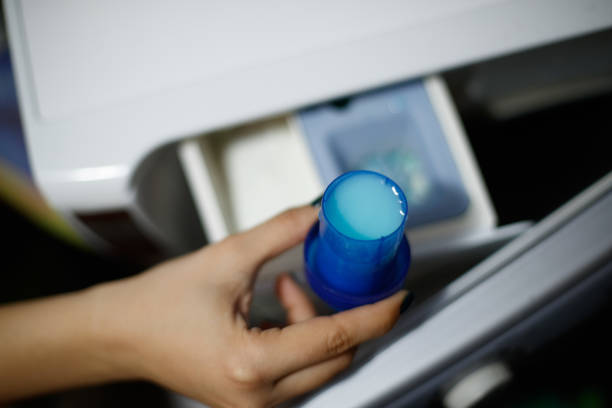 Close-up view at a person's hand holding a fabric softener bottle cap. They're adding it to the container.