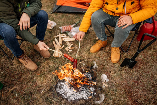 istock Two men sitting around campfire in the forest and baking sausages 1310959549