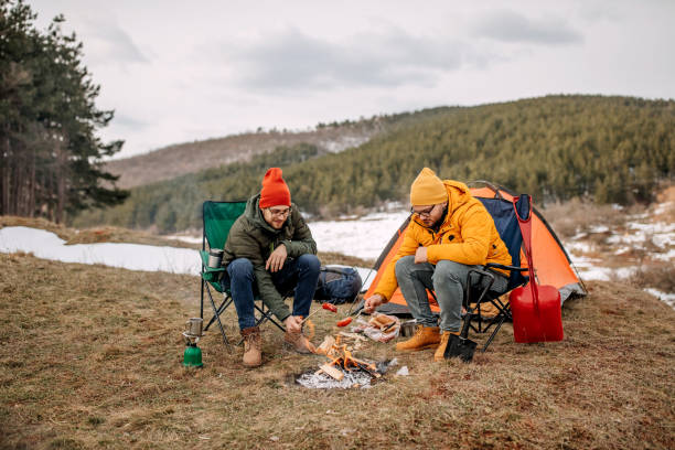 istock Two men sitting around campfire in the forest and baking sausages 1310959705