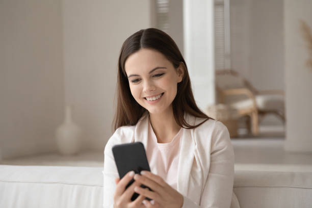 istock Positive young lady sitting on couch enjoying conversation by smartphone 1310961767