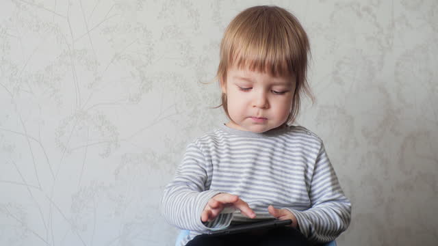 A small child holding a digital tablet and tapping the screen of an electronic device.
