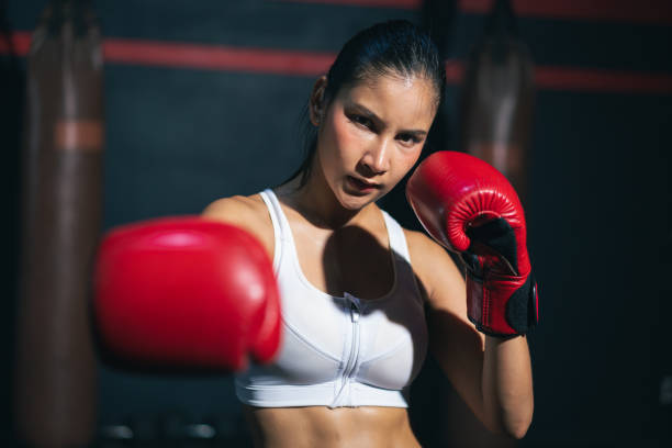 retrato de una boxeadora asiática confiada levantando guardia mirando a la cámara en el gimnasio - boxing womens fotografías e imágenes de stock