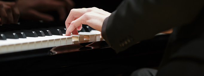 Hands playing the piano keyboard closeup and candle light bokeh background. Male pianist learning to play the piano instrument and beautiful music. Reading sheet music with metronome.