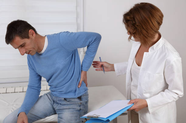 Doctor and Patient suffering from low Back pain during medical exam. Chiropractic, , Physiotherapy concept. stock photo