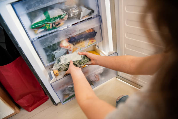 Girl taking raw food from refrigerator Girl taking bag with frozen mixed vegetables from refrigerator. frozen food stock pictures, royalty-free photos & images