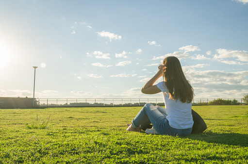 Young woman sitting on the grass with a protective mask during the SARS CoV-2 pandemic season (COVID 19), on the new Orla do Guaiba in Porto Alegre on a beautiful sunset day