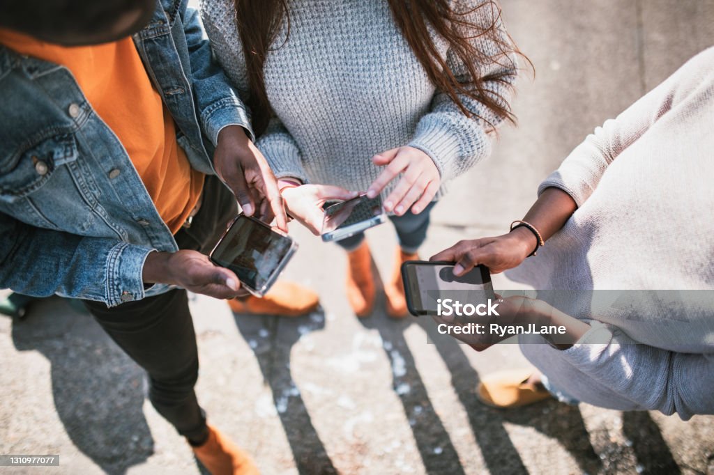Group of Young Adult Friends On Smartphones A multi-ethnic friend group shares things from social media with each other on their various mobile devices.  View from above looking down at the phones. Social Media Stock Photo