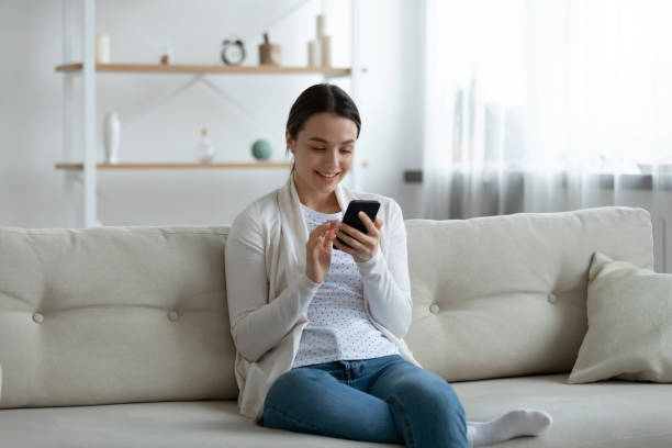 istock Smiling young woman using smartphone, sitting on couch at home 1310977307
