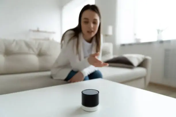 Photo of Close up young woman talking to wireless smart speaker