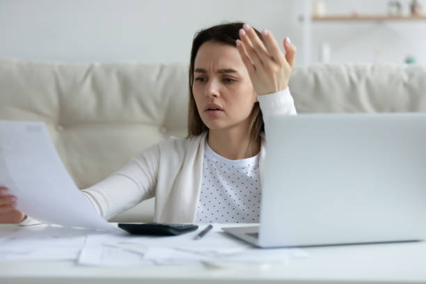 giovane donna irritata che controlla i documenti finanziari, usando il laptop - insolito foto e immagini stock
