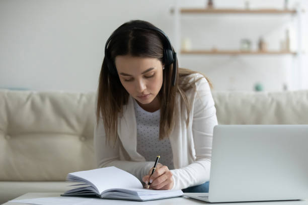 istock Focused young woman wearing headphones using laptop, writing notes 1310977343
