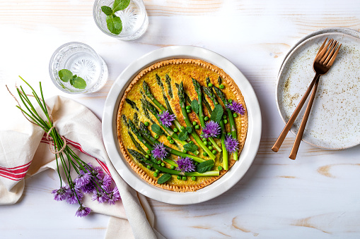 Green asparagus, sweet peas Tart with edible chives flowers or blossoms. Seasonal spring dinner table, overhead view.