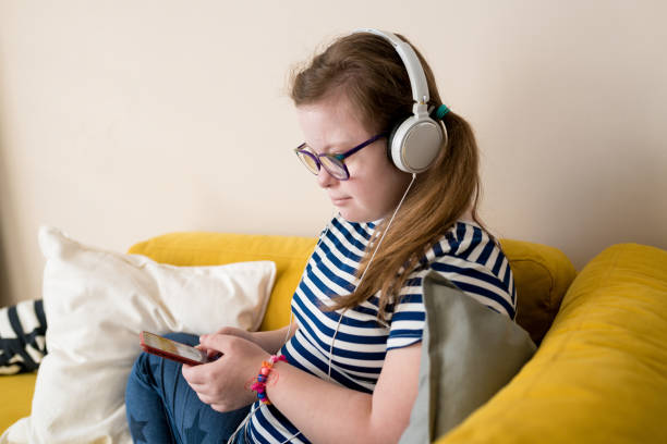 ritratto di ragazza con sindrome di down usando lo smartphone. ragazzo della diversità che ascolta musica in cuffia seduta sul divano a casa. sviluppo audio per bambini con disabilità, educazione inclusiva - the thinker audio foto e immagini stock