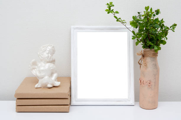 istock Empty white wireframe mock up with glass vase and books on the white table. Wooden frame mockup for your text. 1310982057