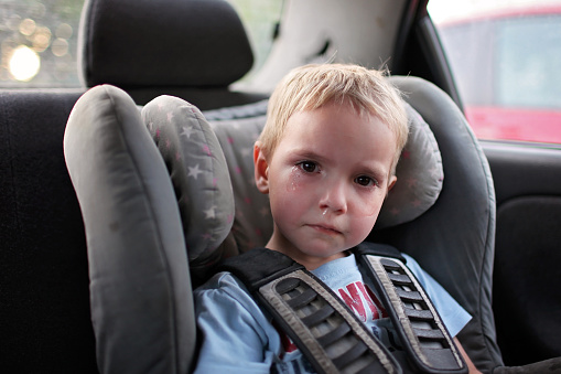 Preschool cute 4-5 years old boy sitting in safety car seat and crying during family travel by car, bad mood, negative emotion, upbringing and family concept, summer outdoor
