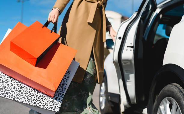 ¡compras exitosas! una mujer shopaholic abriendo la puerta del coche para cargar una gran cantidad de paquetes de diferentes tiendas - shopping bag fotos fotografías e imágenes de stock