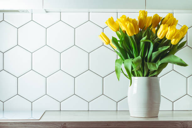 インテリアショット。六角形の白いタイルの背景にキッチンのカウンタートップに白い花瓶の黄色のチューリップブーケ。スペースをコピーする - yellow tulip ストックフォトと画像