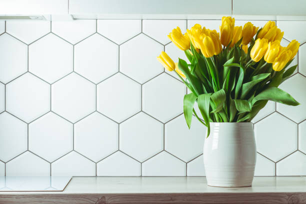 interior shot. yellow tulip bouquet in white vase on kitchen countertop on hexagonal white tile background. copy space - tulip vase flower spring imagens e fotografias de stock