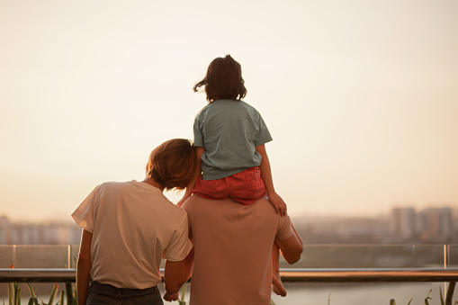 Asian Chinese family with one kids enjoying amazing view of setting sun outdoors in spring.