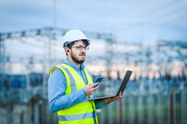 istock Electrical engineer working on a laptop in front of Electricity power station 1311002202