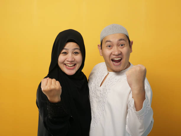 Beautiful Asian muslim couple together standing looked happy and excited doing winner gesture with arms raised, smiling and celebrating victory Beautiful Asian muslim couple together standing looked happy and excited doing winner gesture with arms raised, smiling and celebrating victory success happy malay couple stock pictures, royalty-free photos & images
