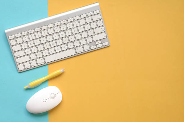 istock Keyboard, mouse and yellow pen on yellow and blue background. Top view. 1311014935