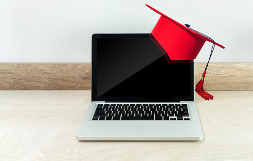 Online education or graduation concept with a laptop on a wooden desk with a red graduate cap