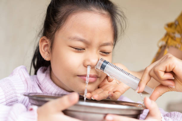 pequeña asiática niña salina nariz de lavado nasal en casa - solución salina fotografías e imágenes de stock