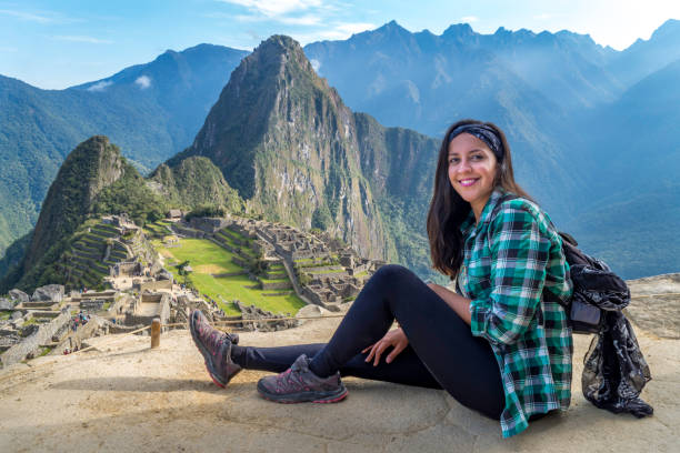 A woman sitting on a Machu Picchu terrace. You can see the ruins of the citadel of Machu Picchu stock photo