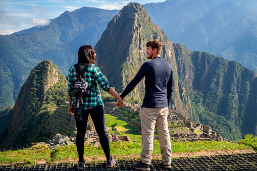 Young couple holding hands looking each other in a terrace of Machu Picchu. One of the Seven Wonders of The New World. UNESCO