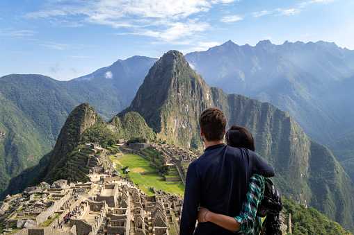 Young couple embracing contemplating the incredible landscape of Machu Picchu. The ruins of the citadel of Machu Picchu and Mount Huayna Picchu are seen