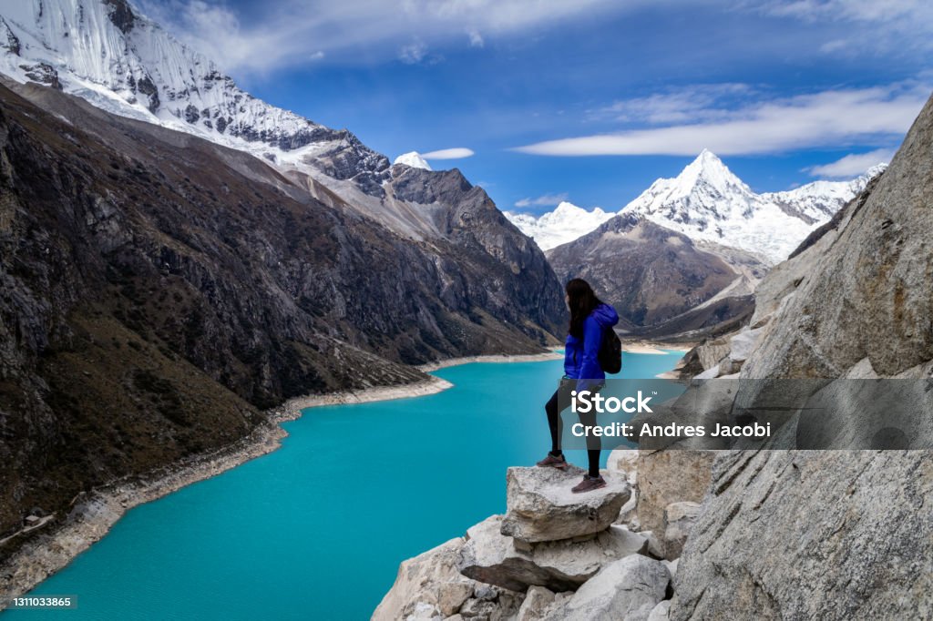 Tourist woman staring at the amazing Lake Paron in Cordillera Blanca of Peru Tourist woman staring at the amazing Lake Paron in Cordillera Blanca of Peru. You can see the beautiful turquoise color of the water and the peak of Piramide mountain behind. Peru Stock Photo