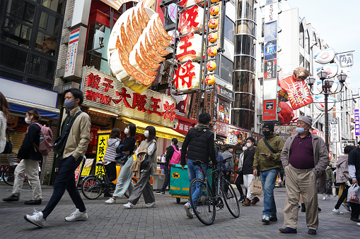 Osaka, Japan - April 1, 2021: Dotonbori in Osaka is busy with people wearing masks shopping and enjoying the street food.