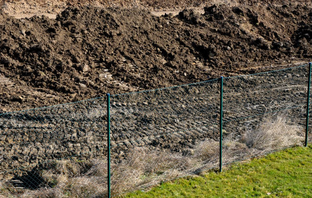 istock bulldozer performs topsoil raking. the land behind the wire fence is now a construction site de the lawn disappears and there is only a pile of soil and heavy construction equipment. The excavator pushes the soil in front of him into a pile 1311035984