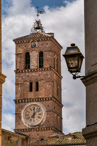 A detailed view of the Romanesque bell tower of the church of Santa Maria in Trastevere, founded by Pope Callixtus I in 222 AD and completed by Pope Julius I around 350 AD.  Trastevere is one of the most iconic districts of the Eternal City, due to the presence of ancient monuments and churches, but also for squares and alleys where it is easy to find typical Italian restaurants, pubs and small art shops. Image in high definition format