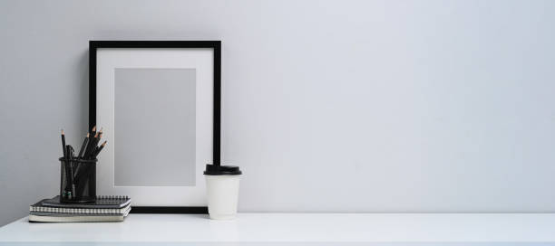 istock Mock up black photo frame, books, coffee cup and pencil holder on white table. Copy space for advertise text. 1311036433