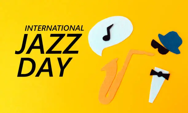 Photo of Silhouette of a musician with a saxophone from which melodie flew out, on a yellow background, cutted out of felt. Flat lay. International Jazz Day
