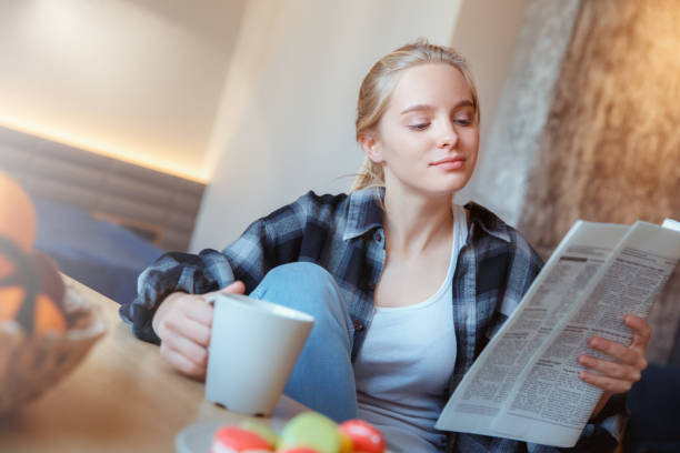お茶を読むニュースを飲んで台所で自宅で若い女性 - young adult reading newspaper the media ストックフォトと画像