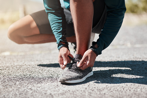 Cropped shot of an unrecognizable man crouching down and tying his shoelaces before going for a run outdoors