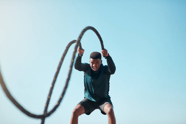 Muscles loading, please wait Cropped shot of a handsome young man using battle ropes during a high intensity workout outdoors endurance stock pictures, royalty-free photos & images