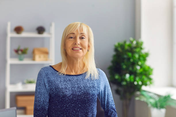 Portrait of a sincere and kind middle aged mature woman who is looking at the camera. Portrait of a sincere and kind middle aged mature woman who is looking at the camera. Woman posing relaxed at home or in the office with a natural face and a confident smile. 55 59 years photos stock pictures, royalty-free photos & images