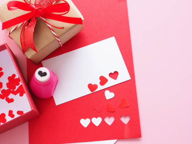 istock White and red paper, heart-shaped punches, red bow tie gift box  and decorations for making a love card on a pink background. 1311044927