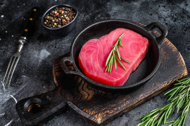fresh raw tuna steak with rosemary in a pan. black background. top view - tuna tuna steak raw freshness imagens e fotografias de stock