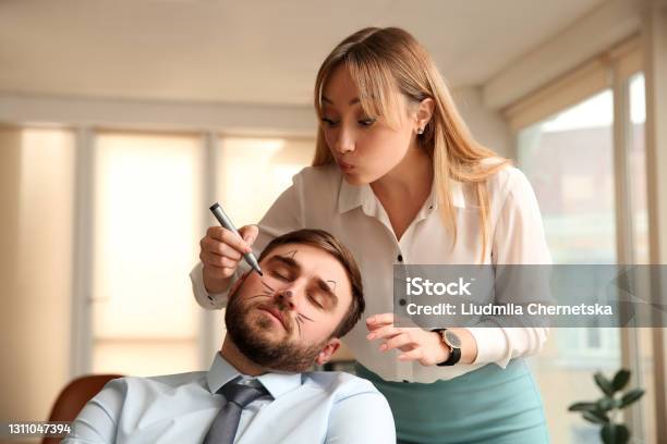 Young Woman Drawing On Colleagues Face While He Sleeping In Office Funny Joke Stock Photo - Download Image Now