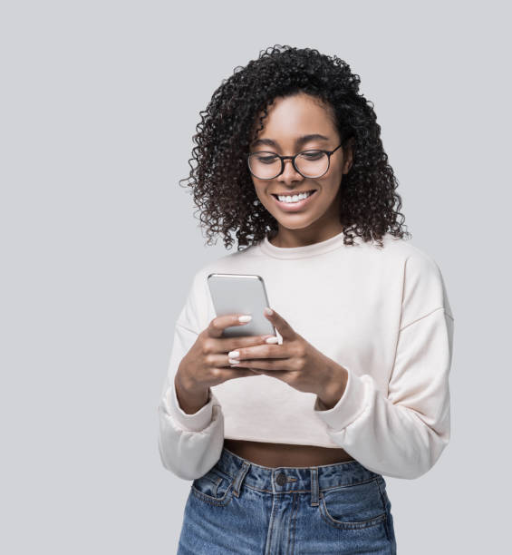 Happy laughing woman student using smart phone Smiling african-american woman looking at mobile phone. People, technology, connection, mobile apps, communication concept happy studio shot stock pictures, royalty-free photos & images